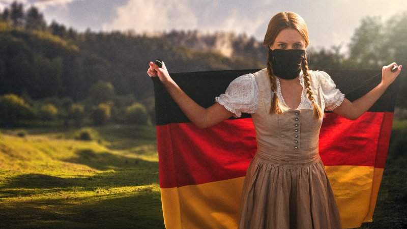 Frau im Dirndl und halb verdecktem Gesicht hält Deutschland-Fahne vor idyllischer Landschaft